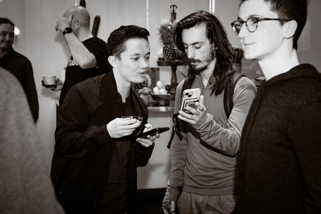 Black and white photo of a guest reading the phone screen of another guest.