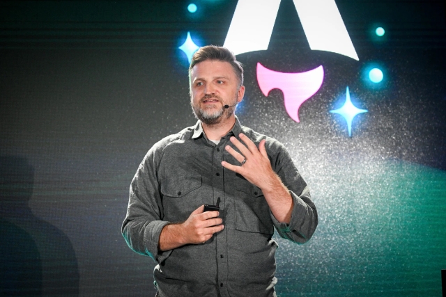 Matthew Phillips speaking on stage. On-screen behind him is the Astro Together logo.