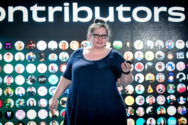 Closeup of Sarah Rainsberger speaking on stage in front of a slide depicting 1,000 Docs contributors.