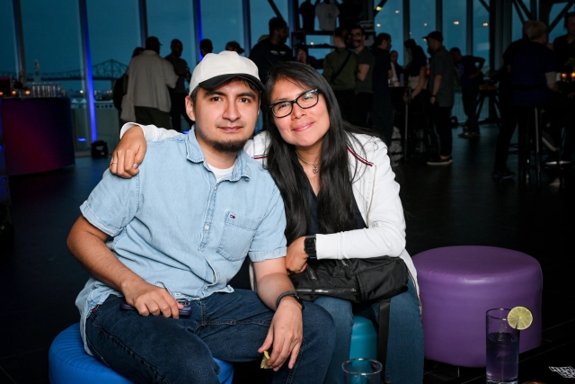 Two guests pose sitting on ottomans. The women has her arm around the man.